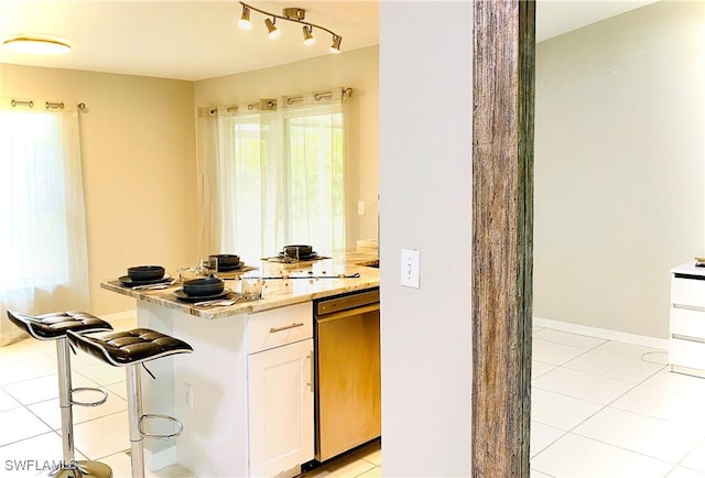 kitchen with light stone counters, light tile patterned floors, dishwasher, white cabinets, and a breakfast bar area