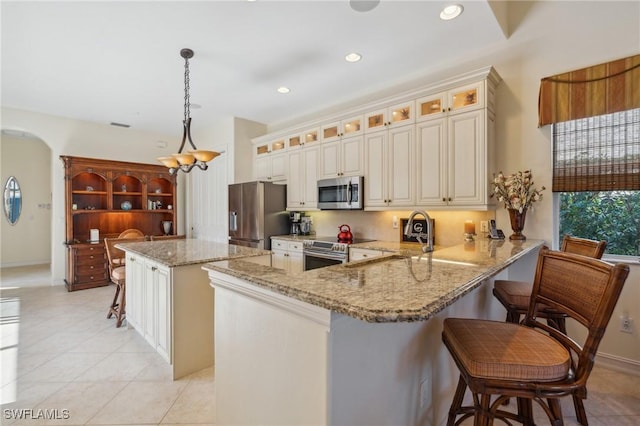 kitchen with decorative light fixtures, a kitchen island, light stone counters, kitchen peninsula, and stainless steel appliances