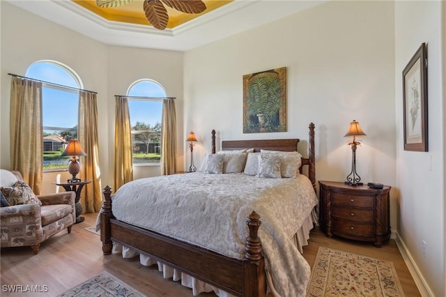 bedroom with light wood-type flooring, a raised ceiling, ceiling fan, and ornamental molding