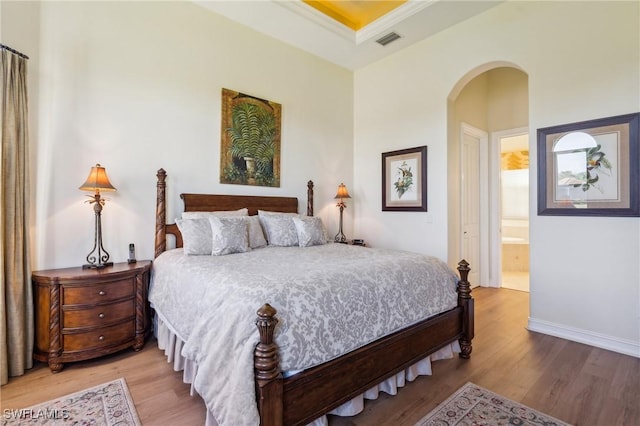 bedroom with wood-type flooring, ornamental molding, and ensuite bath