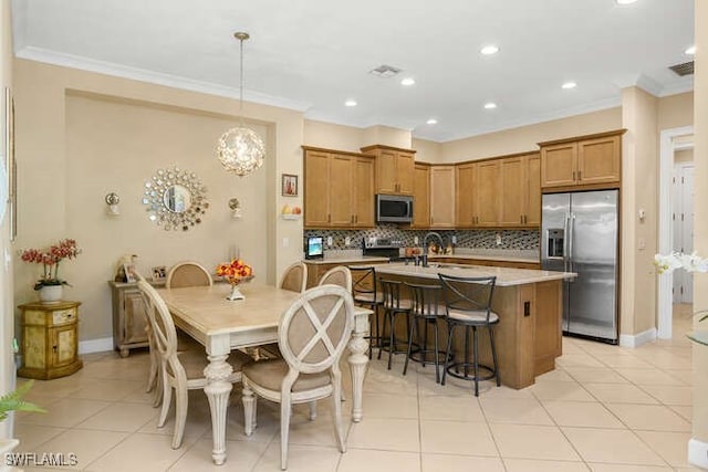 kitchen with tasteful backsplash, stainless steel appliances, crown molding, decorative light fixtures, and an island with sink