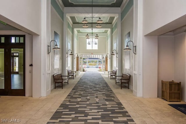 hallway featuring french doors, a towering ceiling, an inviting chandelier, and ornamental molding