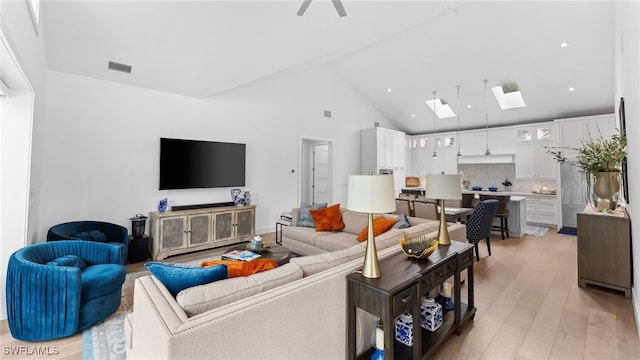 living room featuring high vaulted ceiling, a skylight, and light hardwood / wood-style flooring