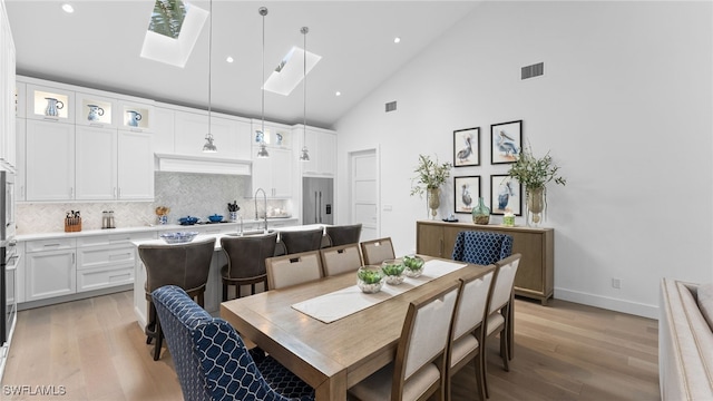 dining area with light hardwood / wood-style floors, sink, high vaulted ceiling, and a skylight