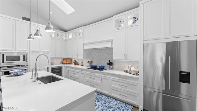 kitchen featuring white cabinets, built in appliances, lofted ceiling with skylight, and sink