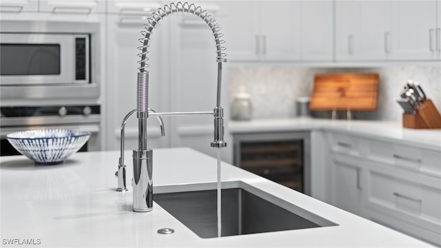 kitchen featuring decorative backsplash, stainless steel microwave, and white cabinets