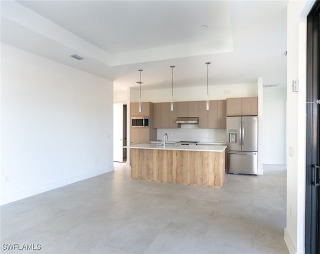 kitchen featuring appliances with stainless steel finishes, a kitchen island with sink, hanging light fixtures, tasteful backsplash, and a raised ceiling