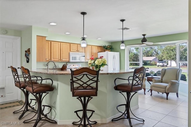 kitchen with light stone countertops, pendant lighting, white appliances, and a kitchen breakfast bar