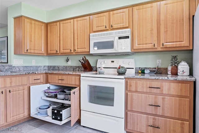 kitchen with dark tile patterned flooring, light stone counters, and white appliances