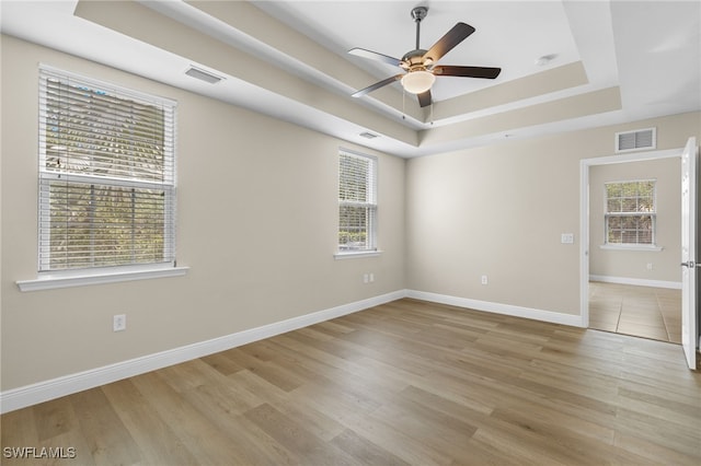 spare room with light wood-type flooring, a tray ceiling, and ceiling fan