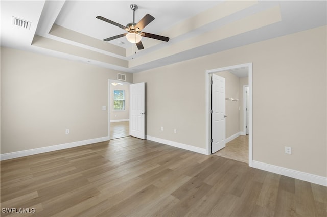 empty room featuring a raised ceiling, ceiling fan, and light hardwood / wood-style flooring