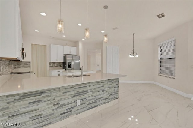 kitchen with pendant lighting, sink, stainless steel refrigerator with ice dispenser, white cabinetry, and a chandelier