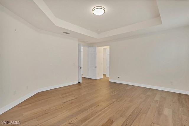 empty room featuring a raised ceiling and light hardwood / wood-style flooring