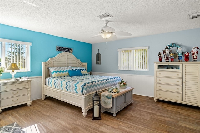 bedroom with hardwood / wood-style floors, ceiling fan, wood walls, and a textured ceiling