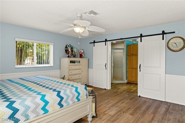 bedroom with dark hardwood / wood-style flooring, a barn door, a textured ceiling, and ceiling fan