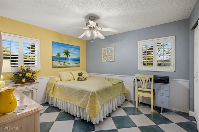 bedroom with a textured ceiling, multiple windows, wooden walls, and ceiling fan