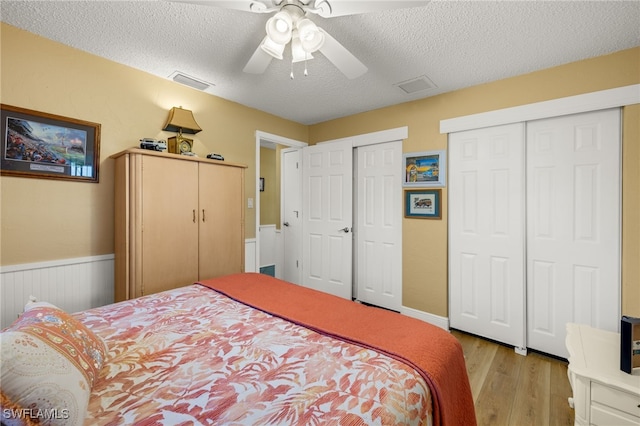 bedroom with a textured ceiling, light wood-type flooring, two closets, and ceiling fan