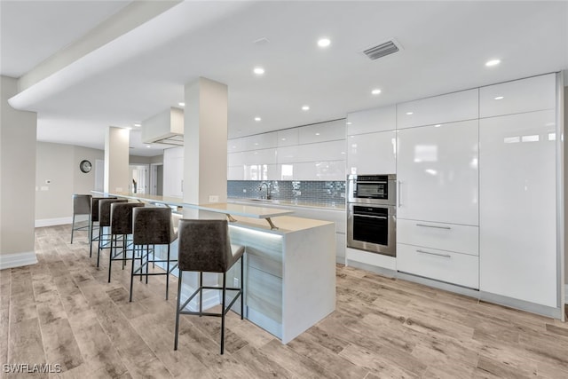 kitchen featuring backsplash, kitchen peninsula, a breakfast bar area, white cabinets, and light wood-type flooring