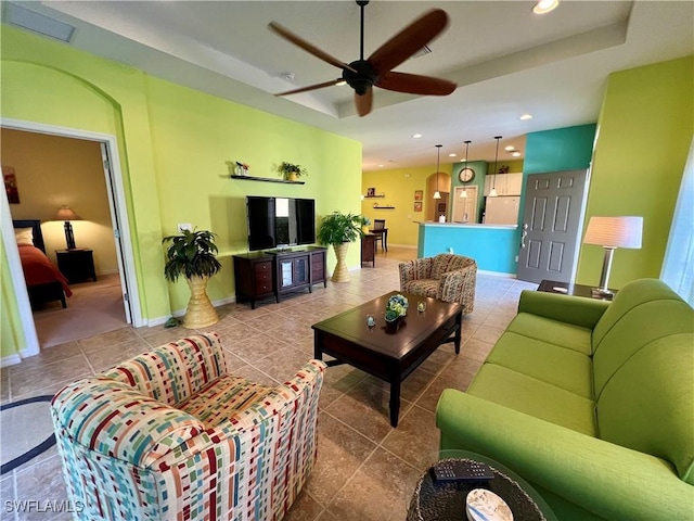 tiled living room featuring ceiling fan and a raised ceiling