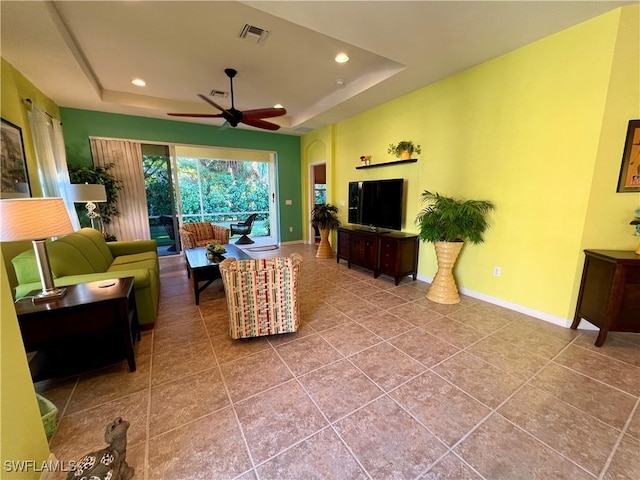 tiled living room with a tray ceiling and ceiling fan