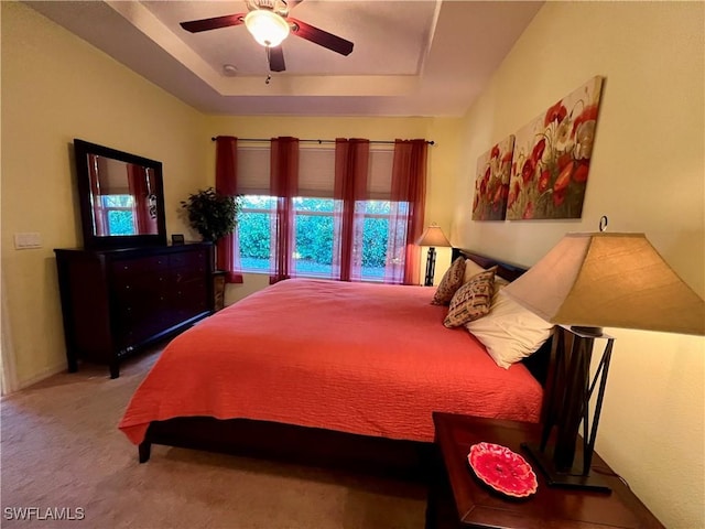 carpeted bedroom featuring ceiling fan and a tray ceiling