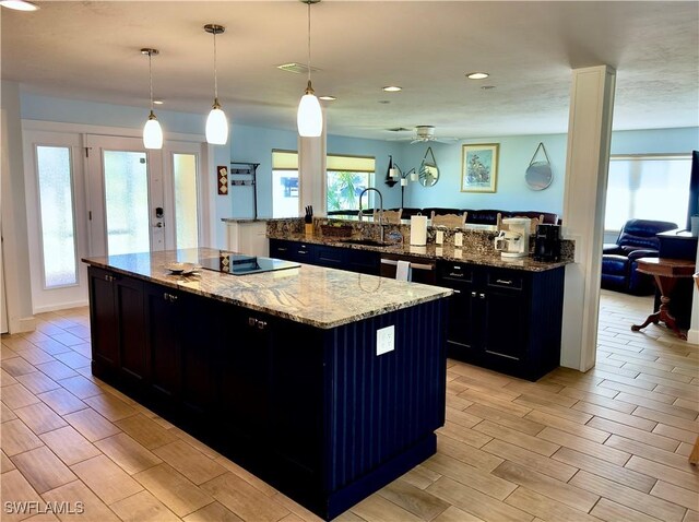 kitchen with decorative light fixtures, sink, light stone counters, a kitchen island with sink, and black electric cooktop