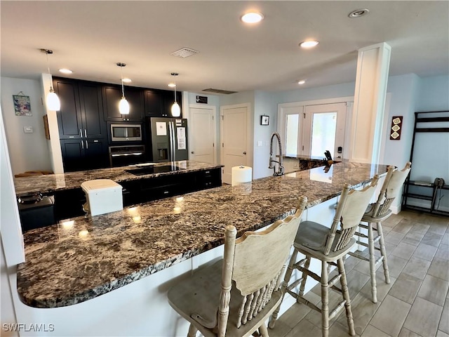 kitchen featuring a spacious island, dark stone counters, hanging light fixtures, and appliances with stainless steel finishes