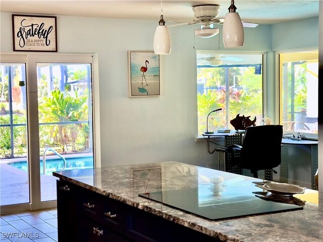 kitchen with decorative light fixtures, light stone counters, black electric stovetop, and a wealth of natural light