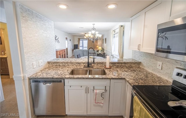 kitchen with white cabinetry, sink, stainless steel appliances, light stone counters, and a notable chandelier