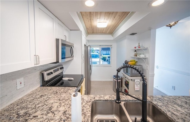 kitchen featuring white cabinets, appliances with stainless steel finishes, a raised ceiling, and light stone countertops