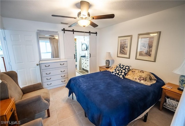 tiled bedroom featuring connected bathroom, a barn door, and ceiling fan