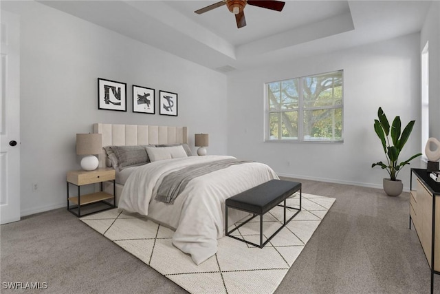 bedroom featuring ceiling fan, light colored carpet, and a tray ceiling