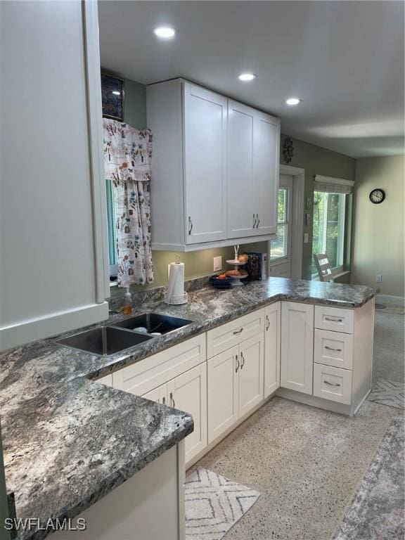 kitchen with kitchen peninsula, sink, white cabinetry, and dark stone countertops