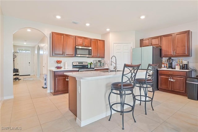 kitchen featuring sink, light tile patterned floors, stainless steel appliances, and a center island with sink