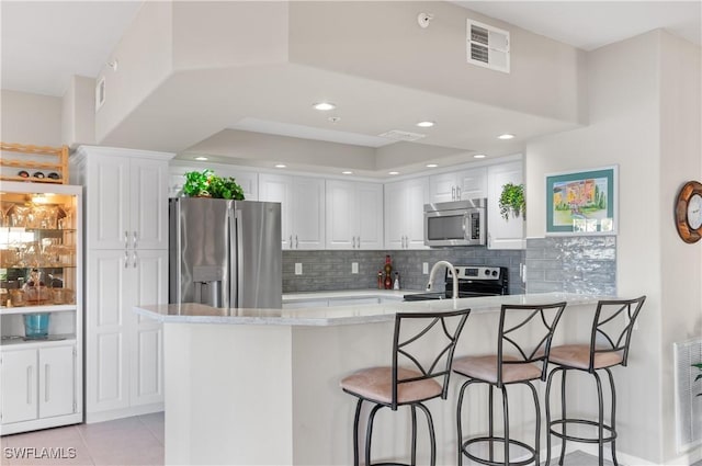 kitchen with light stone countertops, white cabinetry, stainless steel appliances, decorative backsplash, and light tile patterned flooring