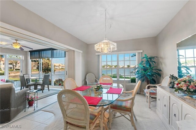 tiled dining area with a wealth of natural light, a water view, and ceiling fan with notable chandelier