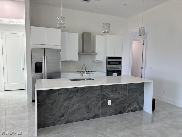 kitchen with sink, white cabinets, hanging light fixtures, a center island with sink, and wall chimney exhaust hood