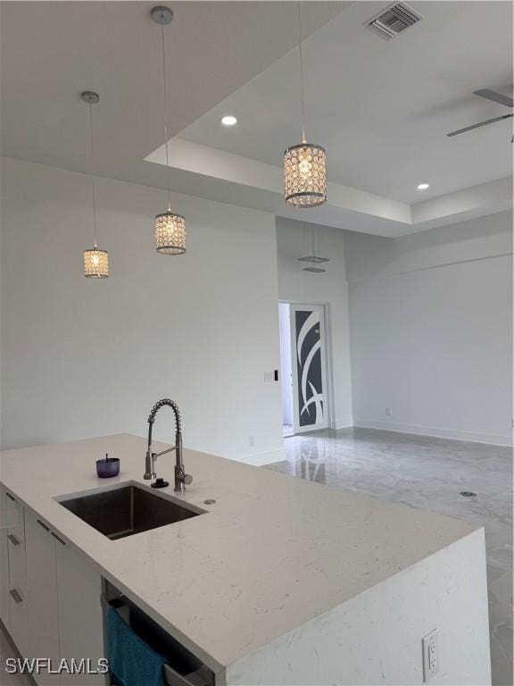 kitchen with ceiling fan, sink, a raised ceiling, an island with sink, and pendant lighting