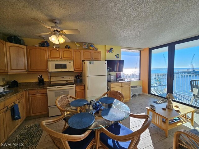 kitchen with white appliances, a wall of windows, ceiling fan, a wall mounted air conditioner, and a textured ceiling