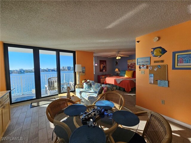 dining room with wood-type flooring, ceiling fan, floor to ceiling windows, a water view, and a textured ceiling