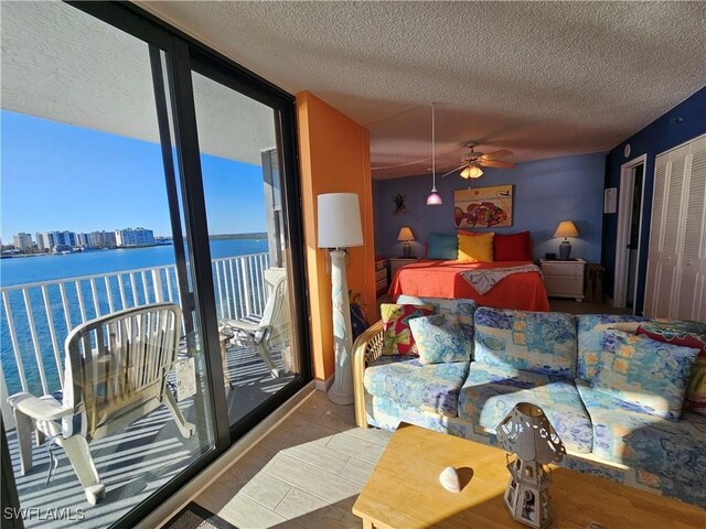 bedroom with floor to ceiling windows, a water view, access to outside, and a textured ceiling