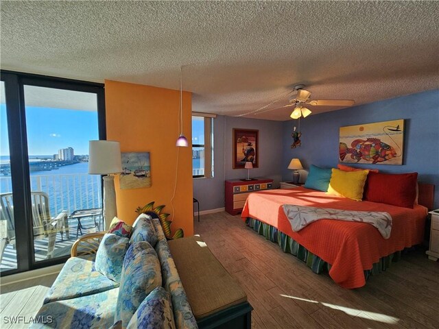 bedroom featuring hardwood / wood-style flooring, ceiling fan, floor to ceiling windows, a water view, and a textured ceiling