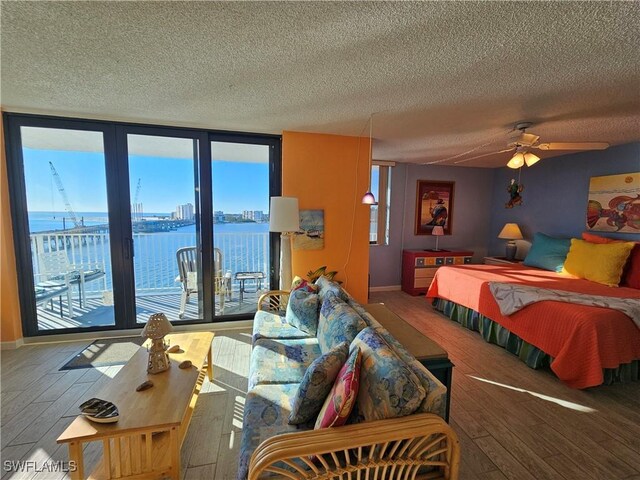 bedroom with expansive windows, a water view, hardwood / wood-style floors, and access to exterior