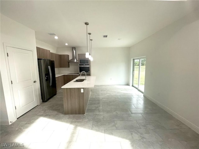 kitchen featuring a kitchen island with sink, hanging light fixtures, sink, wall chimney exhaust hood, and stainless steel appliances