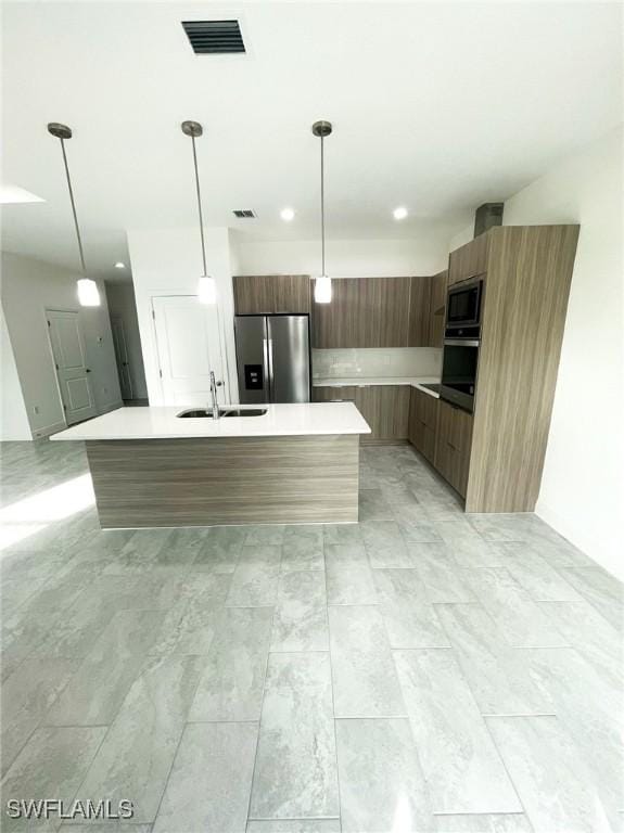 kitchen with hanging light fixtures, appliances with stainless steel finishes, a kitchen island with sink, and sink