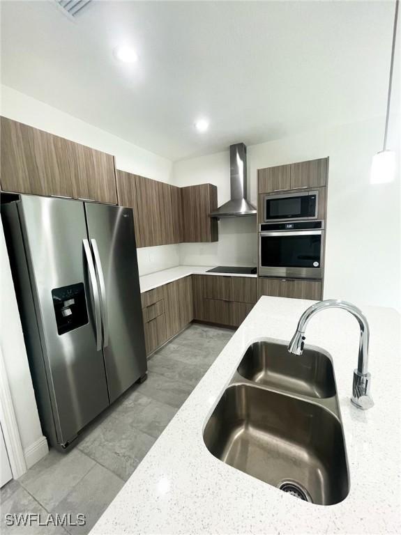 kitchen with sink, stainless steel appliances, wall chimney range hood, light stone counters, and pendant lighting