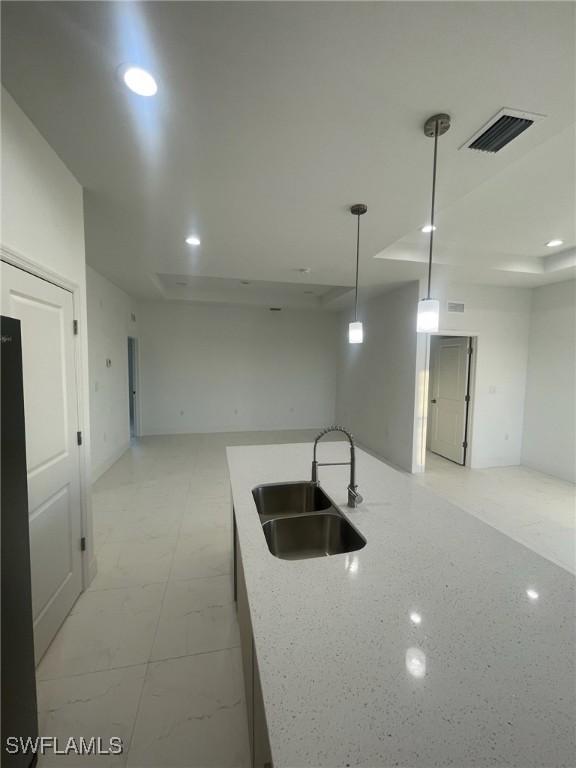 kitchen with light stone counters, hanging light fixtures, and sink