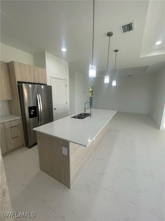 kitchen with decorative light fixtures, stainless steel fridge, sink, and an island with sink