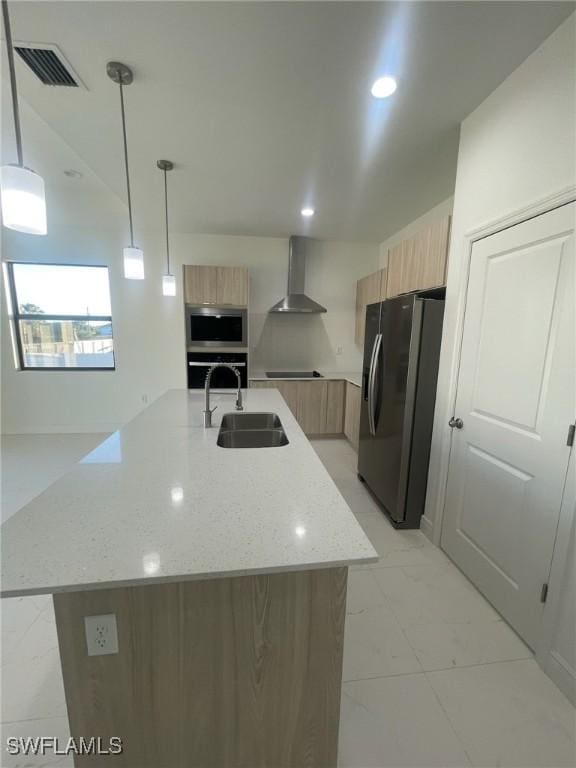 kitchen with appliances with stainless steel finishes, a center island with sink, wall chimney exhaust hood, and pendant lighting