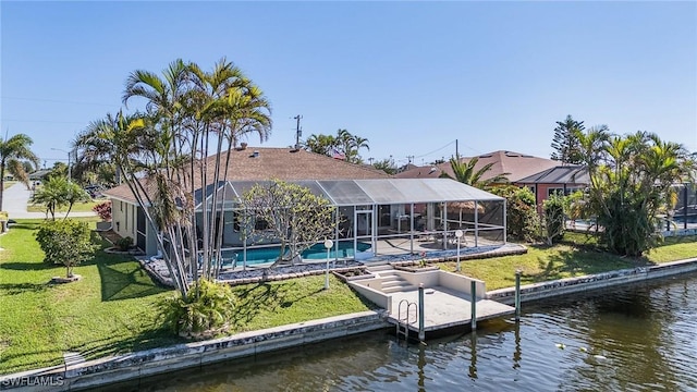 rear view of house with glass enclosure, a water view, and a yard